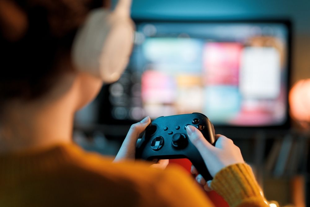 Osoba igra video igru držeći Xbox kontroler ispred televizora