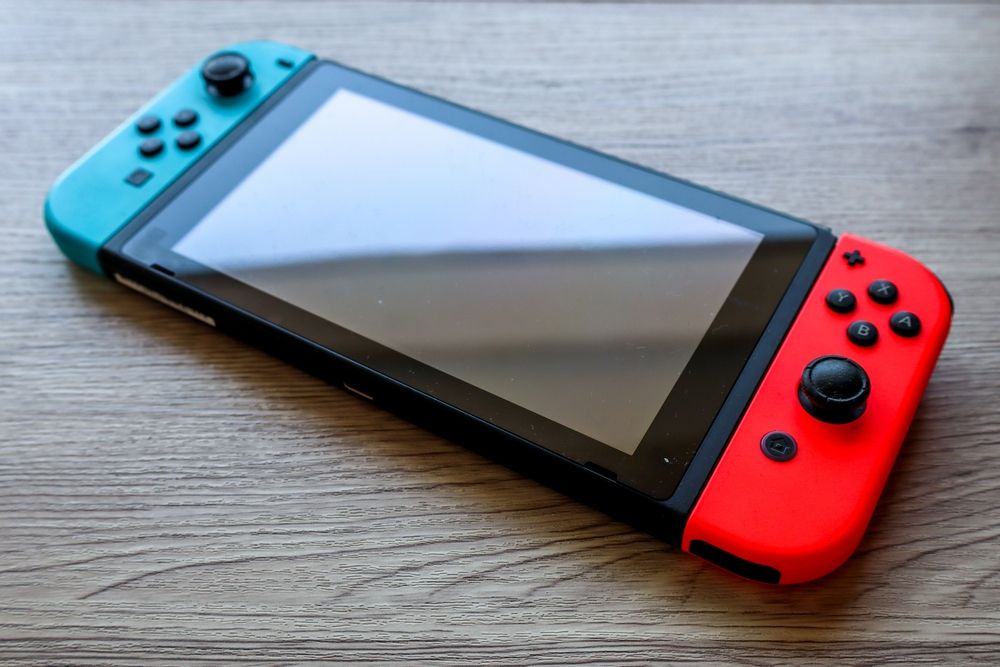 Nintendo Switch konzola sa crvenim i plavim Joy-Con kontrolerima na drvenoj podlozi.